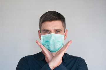Portrait of european dark hair man in surgery face mask in blue shirt on gray background with crossed palms