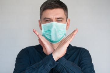 Portrait of european dark hair man in surgery face mask in blue shirt on gray background with crossed palms