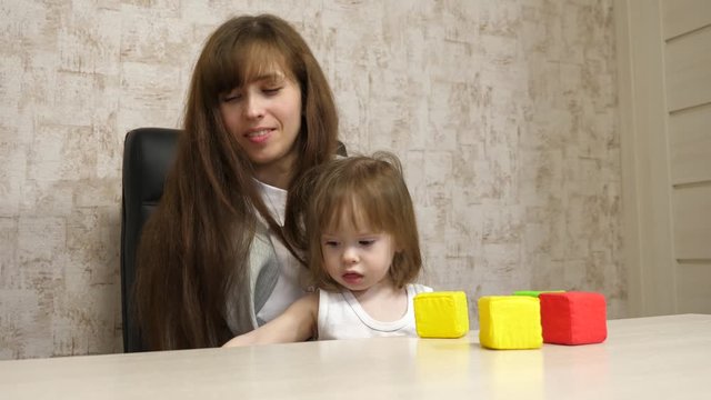 woman works at home with a child. quarantine coronavirus. mother plays with her child in multi-colored cubes at work in office. busy woman is working and resting with a baby in her arms.