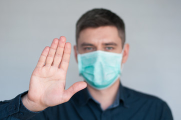 Portrait of european dark hair man in surgery face mask in blue shirt with stop palm on gray background