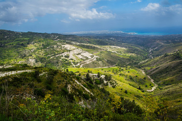 Fototapeta na wymiar Panoramic view of beautiful green calming landscape of Mediterranean valley below clean blue cloudy sky. City of Pafos on the horizon