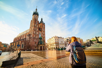 Obraz premium Young stylish woman tourist making photo of the famous St. Mary's Basilica on the Market square during the sunrise in Krakow, Poland