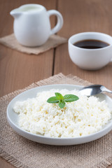 Cottage cheese in a plate, coffee and milk on a wooden table