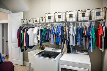 An organized laundry room with many clean shirts being hung to dry above a washer and dryer