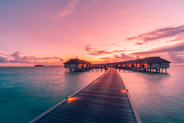 Obraz premium Amazing sunset landscape. Picturesque summer sunset in Maldives. Luxury resort villas seascape with soft led lights under colorful sky. Dream sunset over tropical sea, fantastic nature scenery