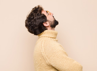 young cool man feeling happy, proud and hopeful, wondering or thinking, looking up to copy space...