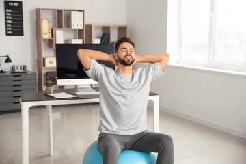 Man doing exercises with fitness ball in office