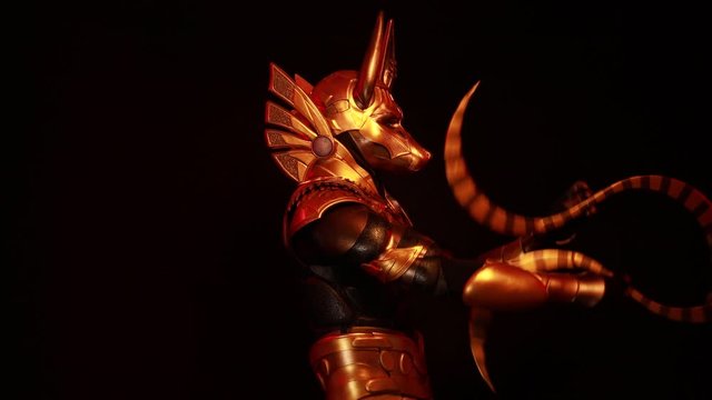 4k video clip, on a black background, a male actor in a suit of an Egyptian mythology character, the golden deity Jackal Anubis, twists buugeng in red light.