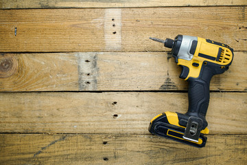 Battery powered impact driver sitting on rough wooden background. 