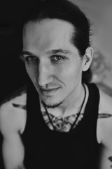 A man in a black T-shirt is standing in a room against a dark background. Soft focus.
