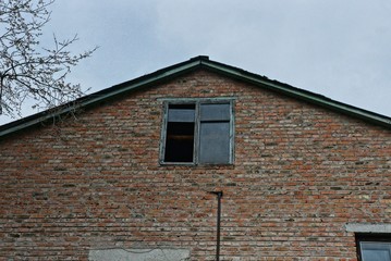 one brown old brick loft with one old window and broken glass against a gray sky