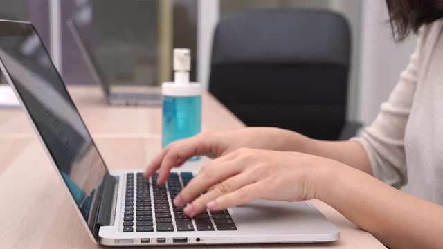 Businesswoman typing laptop and cleaning her hands by alcohol gel hand sanitizer in office or home for prevention of pandemic Covid-19 and Coronavirus, healthcare concept