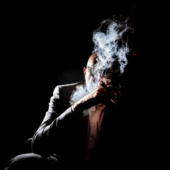 Obraz na płótnie Canvas A man in a cloud of cigar smoke, creative overexposure. Man with a cigarette and smoke, art overexposure.