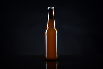Cold unopened bottle of beer with cap on black background. Glass of refrigerated wheat or lager...