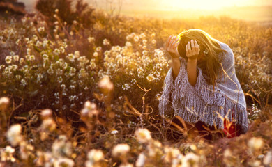 Crouched young girl on a field in flower during sunset