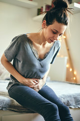 Woman suffering from abdominal pain while sitting on bed.
