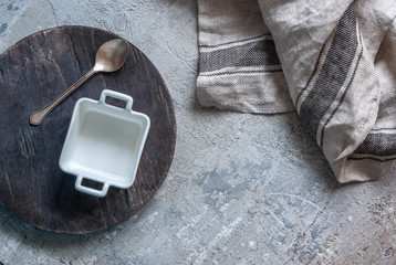 Fototapeta na wymiar White square empty bowl standing on a wooden round board on a concrete worktop. Copyspace, culinary cover.