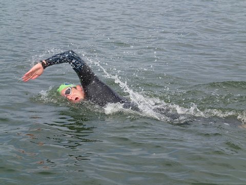 Triathlete open water swimming in lake on a summer's day. Man wearing goggles practicing swim stroke. sport, action, motion and movement