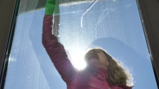 Girl Washes Dirty Window On Balcony Outside With A Rubber Stick On A Sunny Cold Day