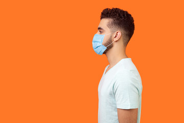 Side view of serious handsome brunette man with surgical medical mask standing with hands down and...