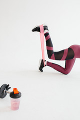 A young woman is engaged in sports with an expander tape. Exercise on the legs.
