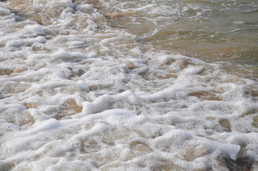 White foam and splashes of the sea running onto a sandy beach