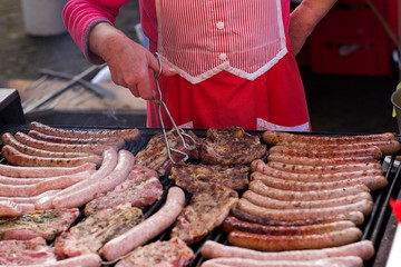 Mann mit Grillzange brät Würstchen und steaks auf einem Holzkohlegrill