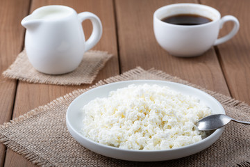 Cottage cheese in a plate, coffee and milk on a wooden table