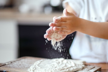 Children's hands knead dough and shake flour from their hands in the kitchen
