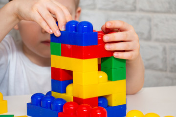 A child in light clothes is building a tower from large plastic blocks. Multi-colored constructor for games. Early childhood development. Home leisure.