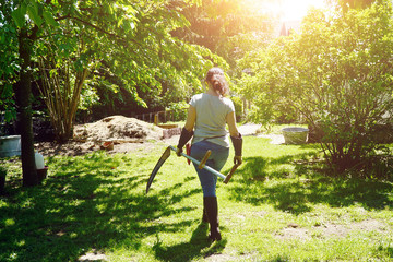 Woman at gardening in the garden mows wild meadow with scythe on a sunny summer day