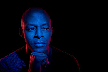 Black man with blue and red light, isolated on black background, looking sideways. Uncertainty...