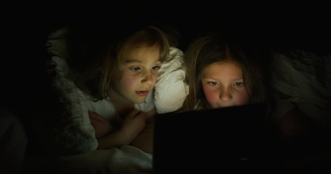 Close up shot of two little girls are using a tablet or smartphone in the dark. Concept: future of web technology, video technology, connections and vision of the future of children with web, gaming
