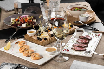dinner table with shrimp, roast beef, salad, cheese platter and wine served at home or at restaurant