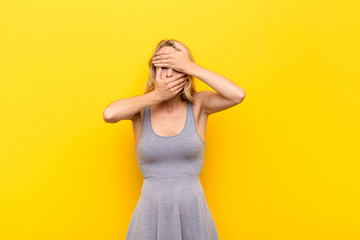 young blonde woman covering face with both hands saying no to the camera! refusing pictures or...