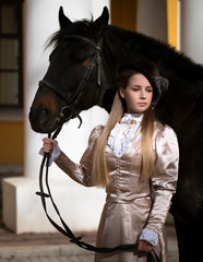 Art photo of a majestic horsewoman in a historical dress with a black hors