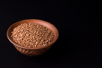 buckwheat in a clay bowl on a black background. copy space