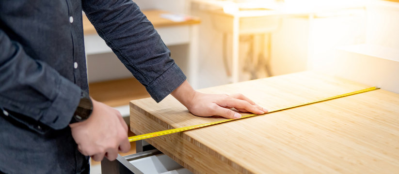 Male hand interior designer using tape measure for measuring size of wooden countertop in modern kitchen showroom in furniture store. Shopping material design for home improvement.