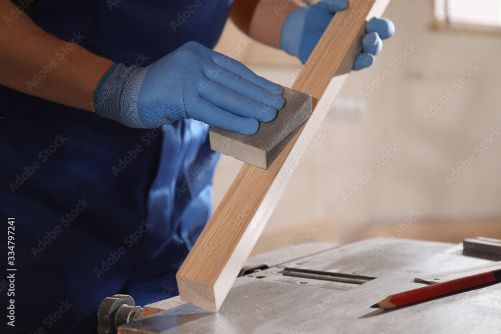 Wall mural Professional carpenter polishing wooden bar in workshop, closeup