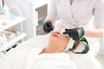 Close-up of unrecognizable beautician putting laser safety goggles on womens face while preparing client for laser surgery