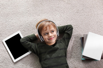 Cute little boy with headphones and tablet listening to audiobook on floor indoors, flat lay