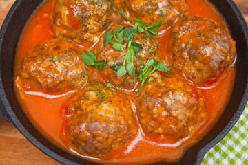 Meat balls in spicy tomato sauce with herbs in a iron pan. Close up. Top view.