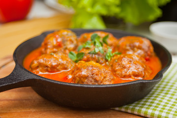 Meat balls in spicy tomato sauce with herbs in a iron pan.