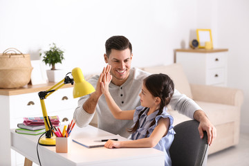 Father and daughter doing homework together at table indoors