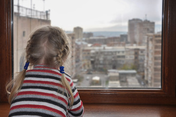 White-haired girl looks out the window. Back view. Quarantined child.