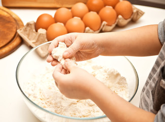 Little child in the home kitchen preparing dough for pizza or another food.