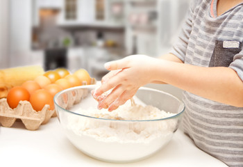 Little child in the home kitchen preparing dough for pizza or another food.