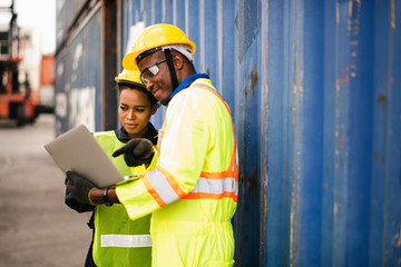 Young African american men and woman worker Check and control loading freight Containers by use computer laptop at commercial shipping dock felling happy. Cargo freight ship import export concept