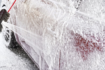 Red car washed in self serve carwash, detail on white soap foam spraying from high pressure hose...