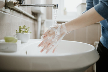 Closeup of a woman washing her hands in bathroom to prevent Covid-19 viral infection. Recommended washing with soap and running water during coronavirus pandemic.